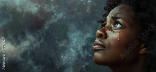 Young black woman looking up praying to God with tears in eyes, being touched by His Grace. Christian and faith concept.