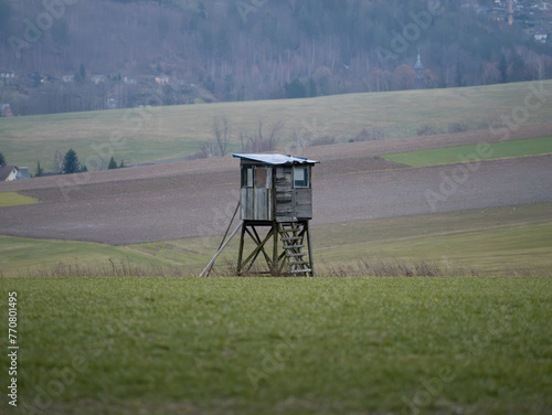 Hunting stand or high seat for hunters in a rural landscape with agricultural fields. Wooden cabin for people to hide and shoot at animals. Countryside in Germany in the morning.