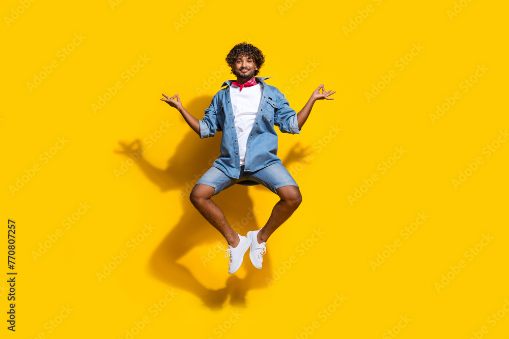 Full length photo of handsome young guy jump yoga meditate om wear trendy denim garment red scarf isolated on yellow color background Full length photo of handsome young guy jump yoga meditate om wear trendy denim garment red scarf isolated on yellow color background