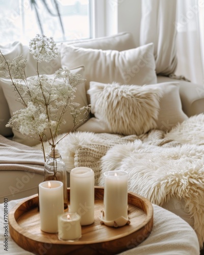 A cozy living room with soft  fluffy white throw pillows and beige blankets on the sofa. A wooden tray holding candles sits beside it  creating an atmosphere of warmth and comfort
