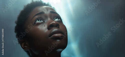 Young black woman looking up praying to God with tears in eyes, being touched by His Grace. Christian and faith concept.