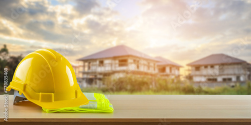 Yellow safety construction helmet on wood table with construction site background © Piman Khrutmuang