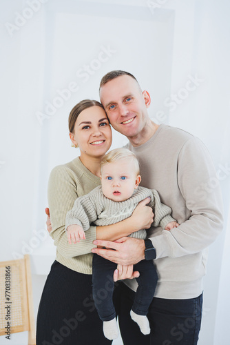 Young family mom and dad with a little six-month-old son on a white background. A married couple hugs their little son. Family relationships