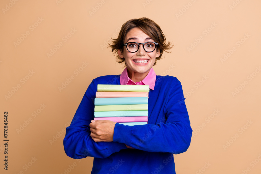 Portrait of positive smart lady beaming smile arms hold pile stack book isolated on beige color background Portrait of positive smart lady beaming smile arms hold pile stack book isolated on beige color background