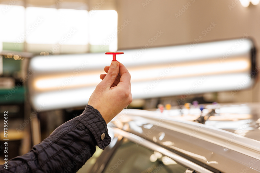 The mechanic holds a T-shaped pin in his hand, which he will later use for car dent removal