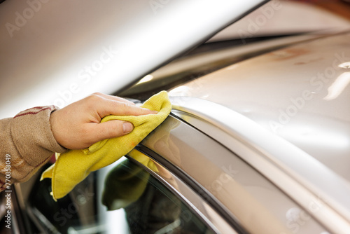 Person cleaning car with yellow cloth on hood and automotive exterior
