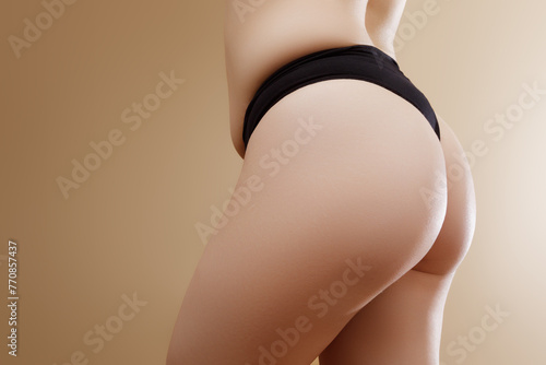 Back view of crop anonymous plump female in black panties with imperfect skin standing against beige background . Stretch marks on female legs. A woman's fat cellulite and a stretch mark