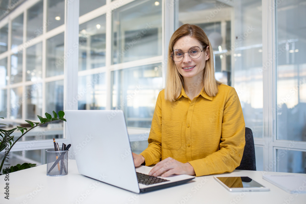 Portrait of a confident, empowered businesswoman smiling happily at her desk in a modern office environment. Portrait of a confident, empowered businesswoman smiling happily at her desk in a modern office environment.