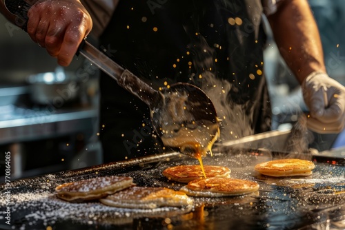 A chef is shown cooking pancakes on a grill, using a spatula to flip them. The batter sizzles, and the pancakes are browning