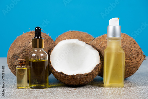 Coconut oil in glass bottles and fruit coconuts on blue background.