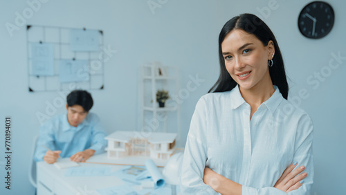 Closeup of female professional architect engineer cross arms with confident while skilled coworker focus on drawing blueprint at table with house model. Creative living and design concept. Immaculate.