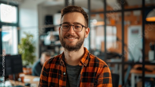 Smiling bearded man in plaid shirt at creative office space. Professional business portrait photo