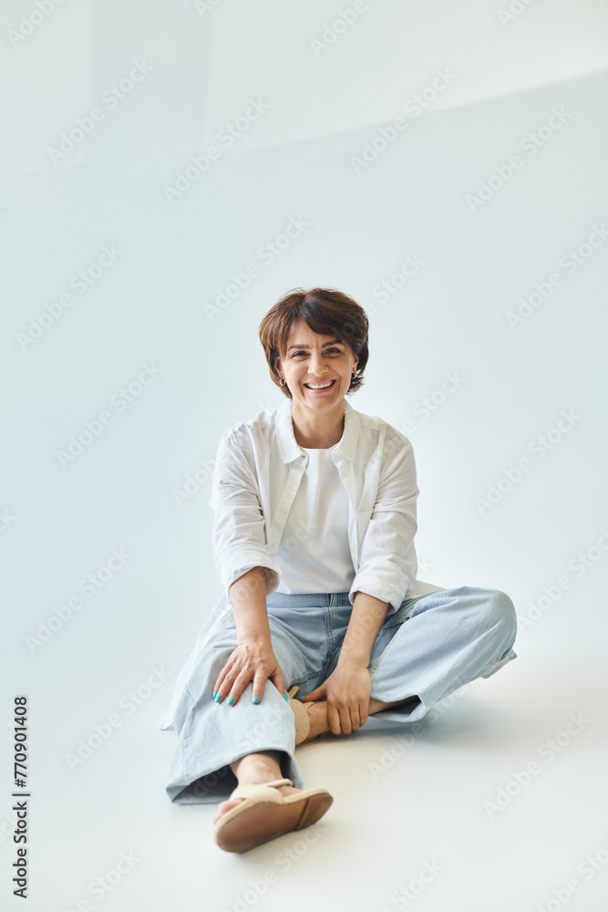 Portrait of mature beautiful smiling woman sitting on grey background and looking at camera Portrait of mature beautiful smiling woman sitting on grey background and looking at camera