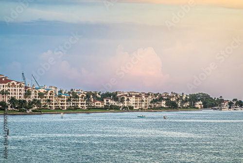Miami, Florida, USA - July 29, 2023: Green tree foliage in front of Luxury condominiums along Fisher Island shoreline under blue evening cloudscape. Small boats on water