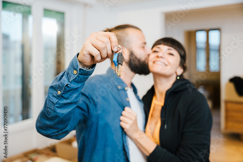 Close-up of the house keys of a young couple who have purchased their first property, in the background the man kisses the girl