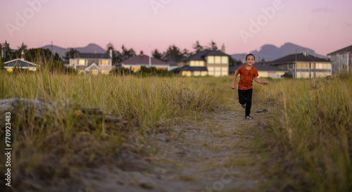 child running towards beach through grass trail