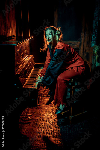 Halloween horrors. A scary clown girl, dressed in a red circus dress, looks at the camera, playing piano