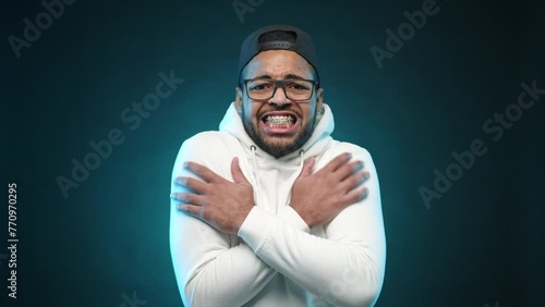 A man in a white hoodie is shivering, wrapping his arms tightly around himself to stay warm against a chilly blue background. Camera 8K RAW.  photo