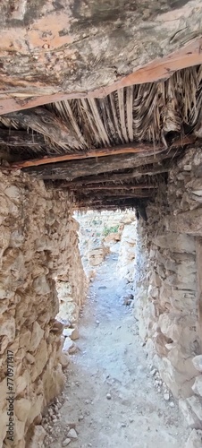 The perspective from a gap in a stone wall reveals the remnants of The balconies of Ghoufi, an ancient Berber village, with houses made of stone and clay, Batna. Algeria photo