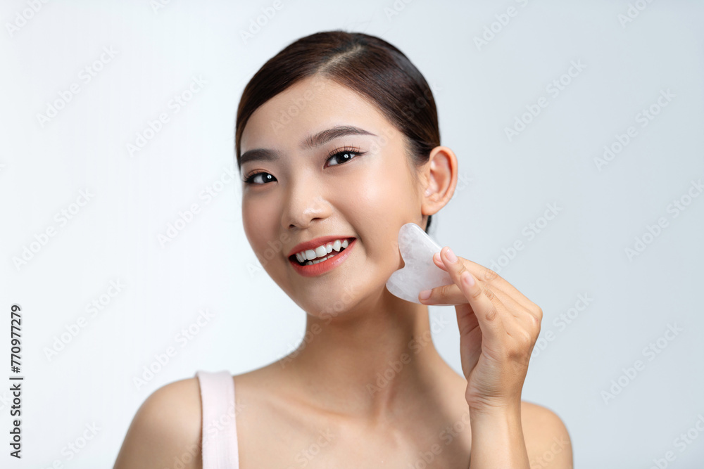 Young Asian woman smiles as she massages her face using a face stone Young Asian woman smiles as she massages her face using a face stone