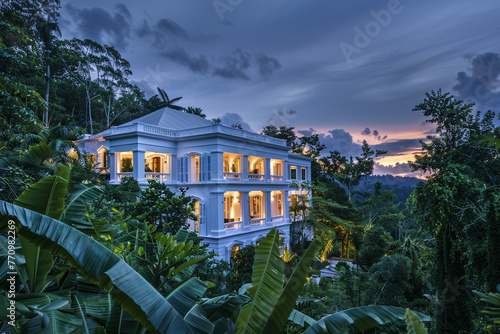 Luxurious white estate surrounded by lush foliage under a spellbinding sky at dusk, showcasing the intersection of nature and modern design. © Imama Hashim
