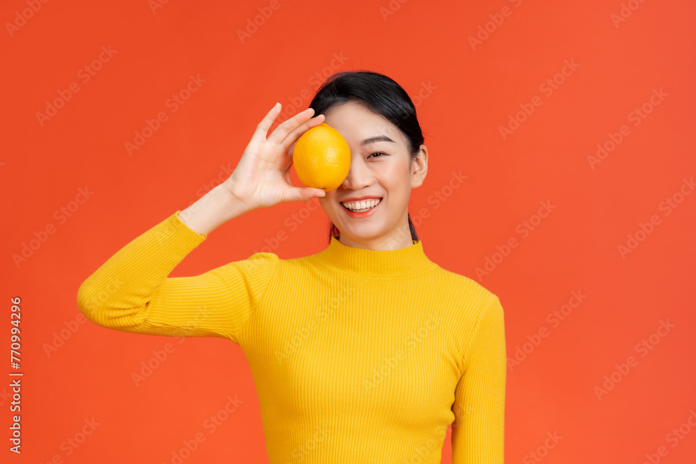 Smiling woman holding orange in front of eye Smiling woman holding orange in front of eye