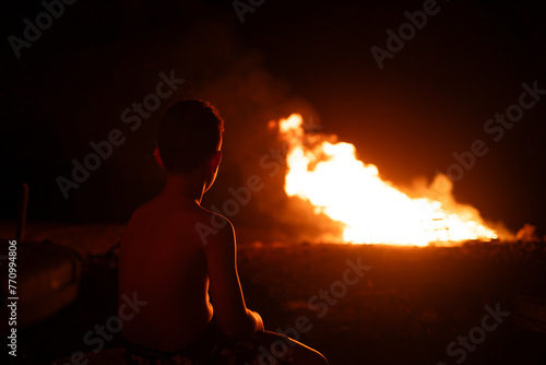 A teenager stares at a controlled fire at night photo