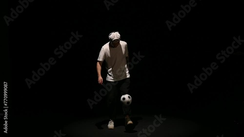 A young man throws a soccer ball on a black background. Football player shows tricks with the ball. Freestyler hits a black and white ball on a dark background. High quality FullHD footage photo