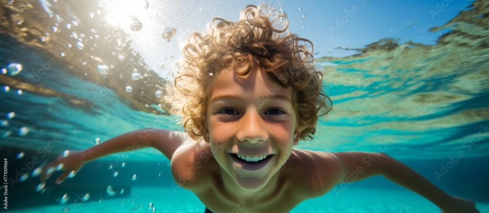 The young boy, with aqua hair flowing, swims happily underwater in the pool, his head surrounded by water as he smiles with joy and leisure