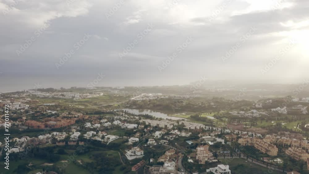 Aerial of countryside houses with small lake in the background in green landscape under cloudy sky Aerial of countryside houses with small lake in the background in green landscape under cloudy sky