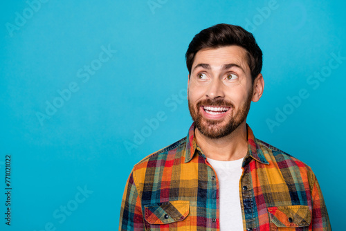 Portrait of positive cheerful pleasant guy with stubble wear plaid shirt look at nice offer empty space isolated on blue color background