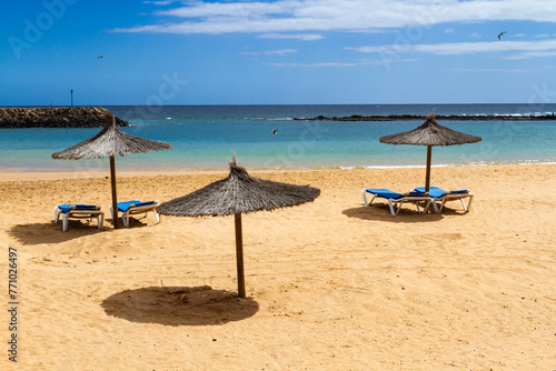 An empty beach in the off-season with straw umbrellas and blue sun lounger.  Playa del Castillo in  Caleta de Fuste, Fuerteventura, Canary Islands, Spain,
