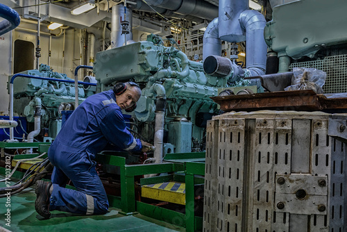 Marine Engineer in blue overall working in Engine room of ship. Work at sea. Motorman.