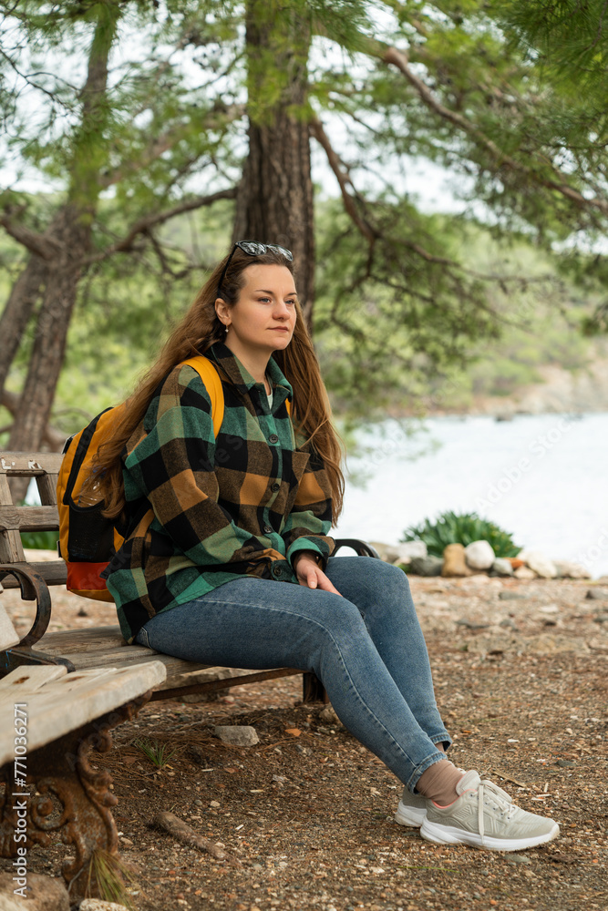 The traveler with a backpack rests on a bench in the forest by the sea. The traveler with a backpack rests on a bench in the forest by the sea.