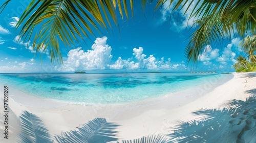 A tropical ocean beach landscape with bright blue water and waves reaching the sand. Beautiful blue sky and clouds.