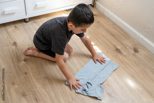 Young Boy Folds T-Shirt Independently, Breaking Gender Norms. photo