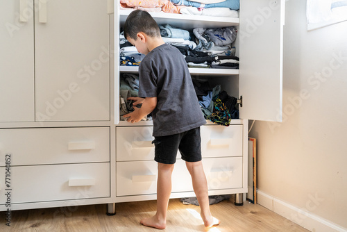 Young Boy Organizes Clothes in Open Wardrobe. photo