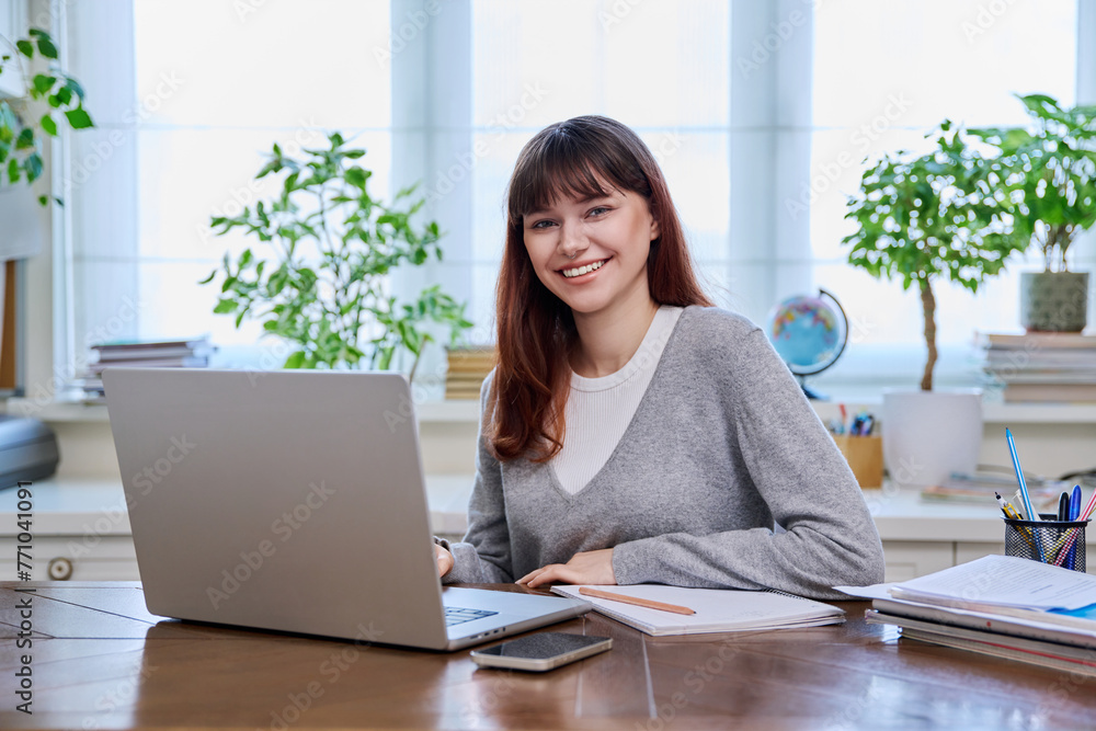 Young female college student studying at home using laptop, looking at camera Young female college student studying at home using laptop, looking at camera
