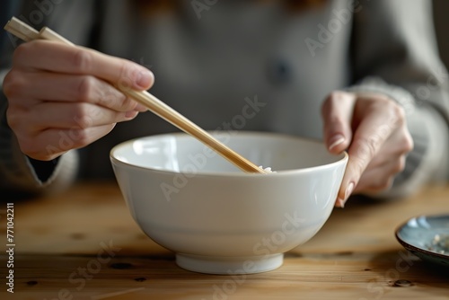 A person is eating noodles with chopsticks. The noodles are in a white bowl
