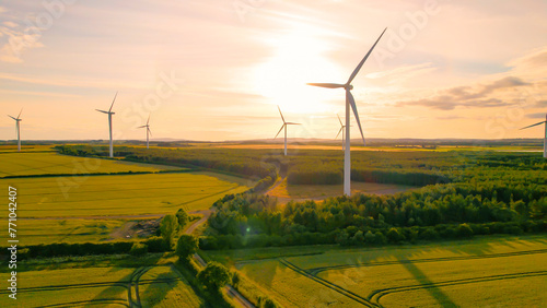 AERIAL, LENS FLARE: Colourful sunset sky above farmland and spinning windmills