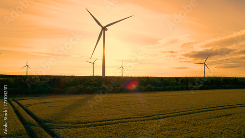 AERIAL, SILHOUETTE: Golden sunrise with modern windmills rising above fields