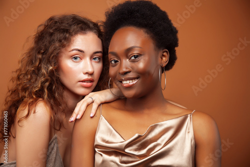 two pretty girls african and caucasian blond posing cheerful together on brown background, ethnicity diverse lifestyle people concept