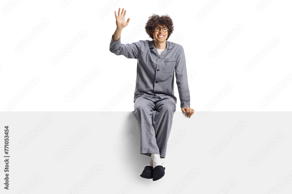 Young man in pajamas and slippers sitting on a blank panel and waving Young man in pajamas and slippers sitting on a blank panel and waving