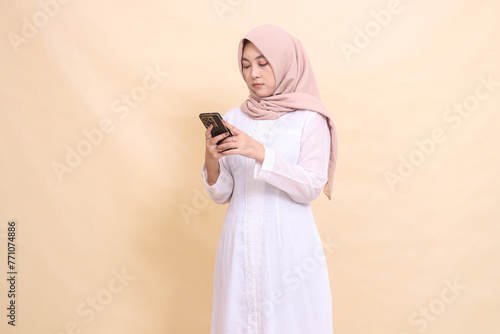 Asian Muslim woman wearing a hijab operates a cellphone gadget in her hand. Lifestyle, technology and promotion concept