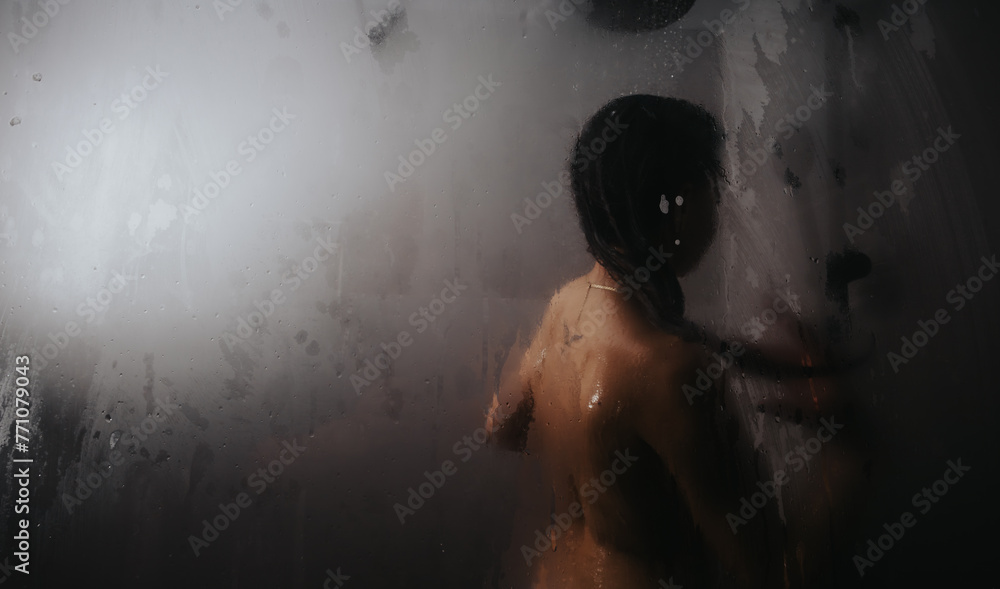 A contemplative moment as a silhouette of a person is seen through the foggy, steamed-up glass of a shower.