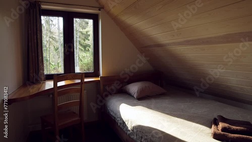 Cozy Bedroom with One Single Bed and Very Small Desk and Chair. Roof Room in Warm Colors with Sloped Roof Ceiling Finished with Wooden Planks.