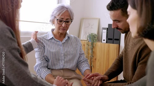 Diverse people sitting in circle receiving support during a therapy session. Young adult man and woman calming depressed senior woman partner in professional guidance meeting. 