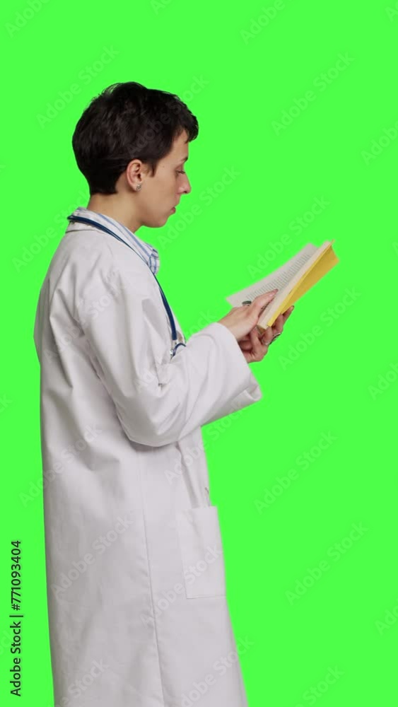 Profile Medic specialist reading a healthcare literature book to develop her medical expertise in the industry, stands against greenscreen backdrop. Clever doctor in white coat enjoys lecture. Camera Profile Medic specialist reading a healthcare literature book to develop her medical expertise in the industry, stands against greenscreen backdrop. Clever doctor in white coat enjoys lecture. Camera