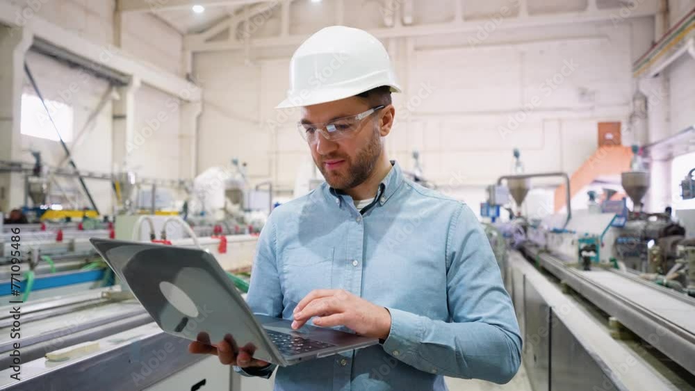 Factory chief engineer in a hard hat is using a laptop with an engineering software Factory chief engineer in a hard hat is using a laptop with an engineering software