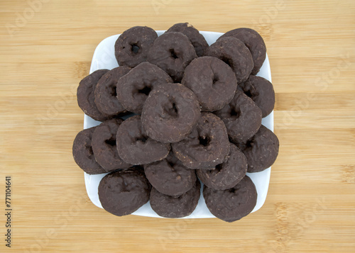 close up on a square plate with round chocolate donuts on a light wood table.